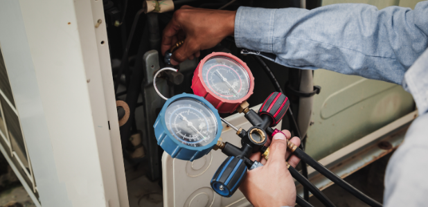 An Air conditioner technician is using a manifold gauge to check the refrigerant in the system to inspect and repair the outdoor air compressor.