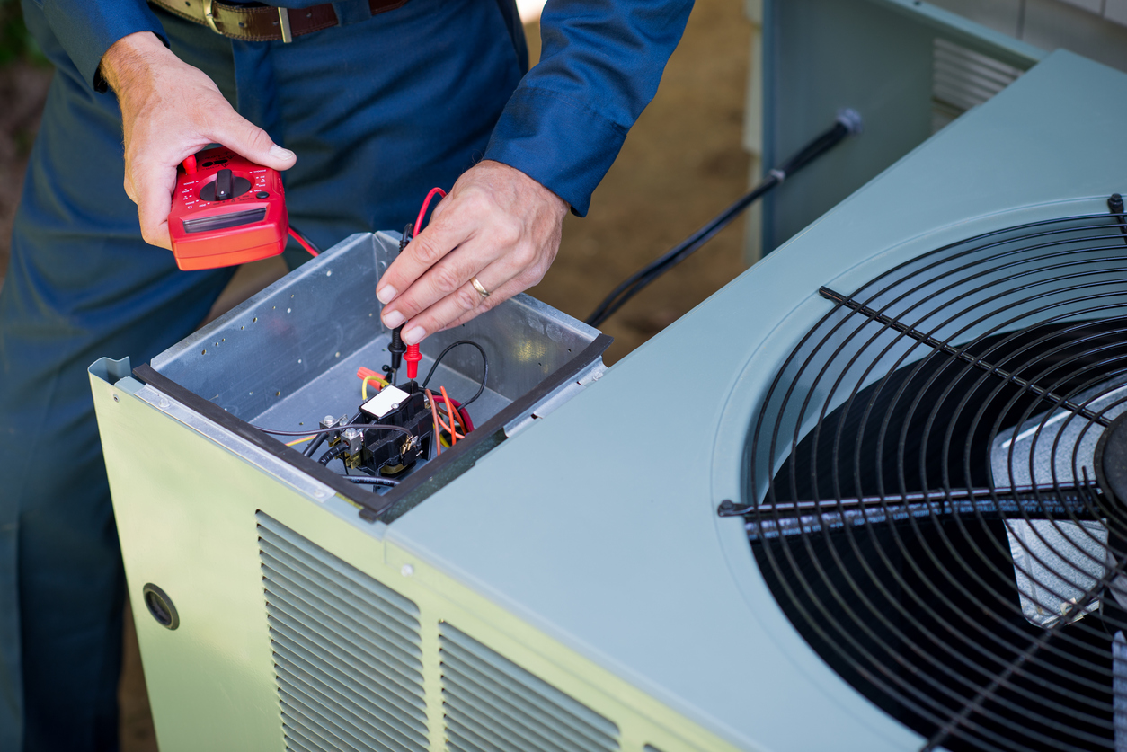 An HVAC technician tests the electrical components of an outdoor unit to determine whether it needs repair or replacement.